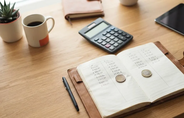 Registre fictif à deux colonnes, deux pièces et calculatrice sur un bureau.